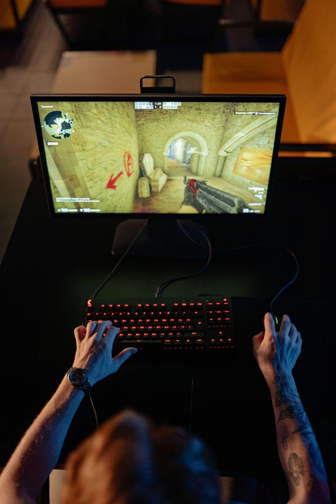 Top-down view of a gamer playing on a PC with a glowing keyboard in a dark room.